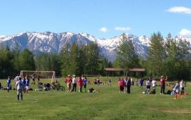 Snow capped mountains and blue sky behind green grass soccer field with players. 