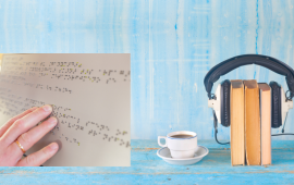 blue room with hand reading braille, coffee cup, and headphones over books