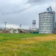 green grass with a cloudy sky, a round gray grain storage building, and palmer water tower. 