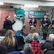 large library room with a seated crowd and Celtic pipes and drums band playing