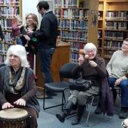 a dozen people seated, playing bongo drums in the library