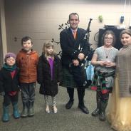 A man in Celtic dress holding a bagpipe posing with five children