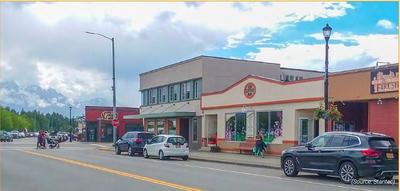 Buildings on main street in a small town, with people crossing the street and parked cars.