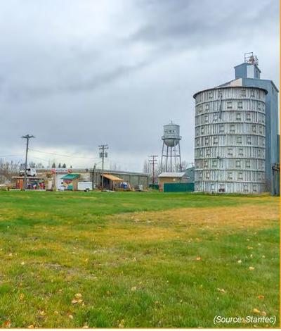 green grass with a cloudy sky, a round gray grain storage building, and palmer water tower. 